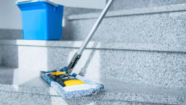 Feuchter Bodenwischer auf grauem Marmortreppe mit blauem Eimer im Hintergrund.