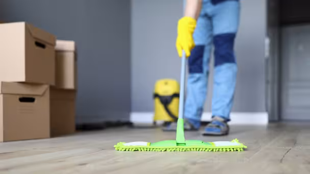Person wischt mit gr&uuml;nem Wischmopp und gelben Handschuhen hellen Boden.